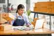© David - Young Asian entrepreneur SME woman checking product on stock take note with a laptop. Small business owner working at home. Check address on the parcel SME online start up freelance concept.