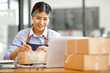 © David - Young Asian entrepreneur SME woman checking product on stock take note with a laptop. Small business owner working at home. Check address on the parcel SME online start up freelance concept.