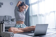 © amenic181 - Sporty young Asian woman exercising at home, watching fitness video on Internet or having online fitness class, using laptop, living room interior, copy space