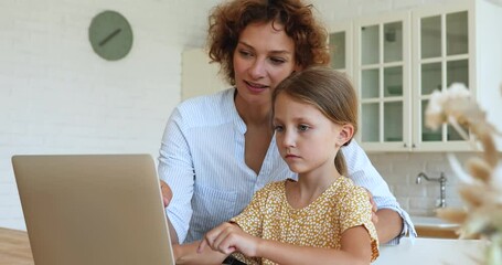 Wall Mural - Happy caring young mother teaching small 7s kid daughter using computer software applications at home. Smiling two female generations family enjoying studying in educational software programs.