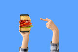 Fototapeta Tęcza - Hands of woman with mobile phone buying burger online against blue background