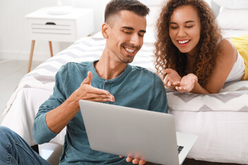 Wall Mural - Young couple using modern laptop in bedroom