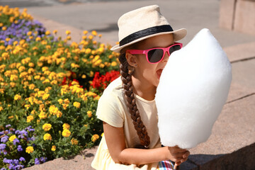 Wall Mural - Cute little girl eating cotton candy outdoors