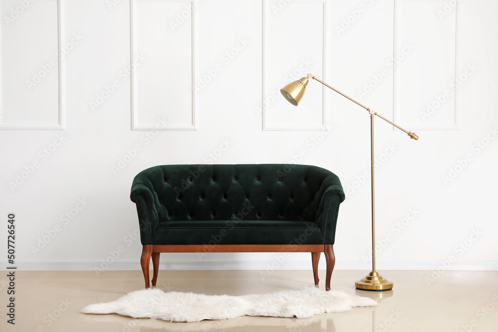 Stylish sofa and modern lamp near light wall