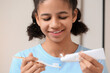 © Pixel-Shot - African-American teenage girl applying tooth paste onto brush in bathroom, closeup