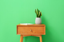 Wooden Table With Houseplant And Notebook Near Green Wall