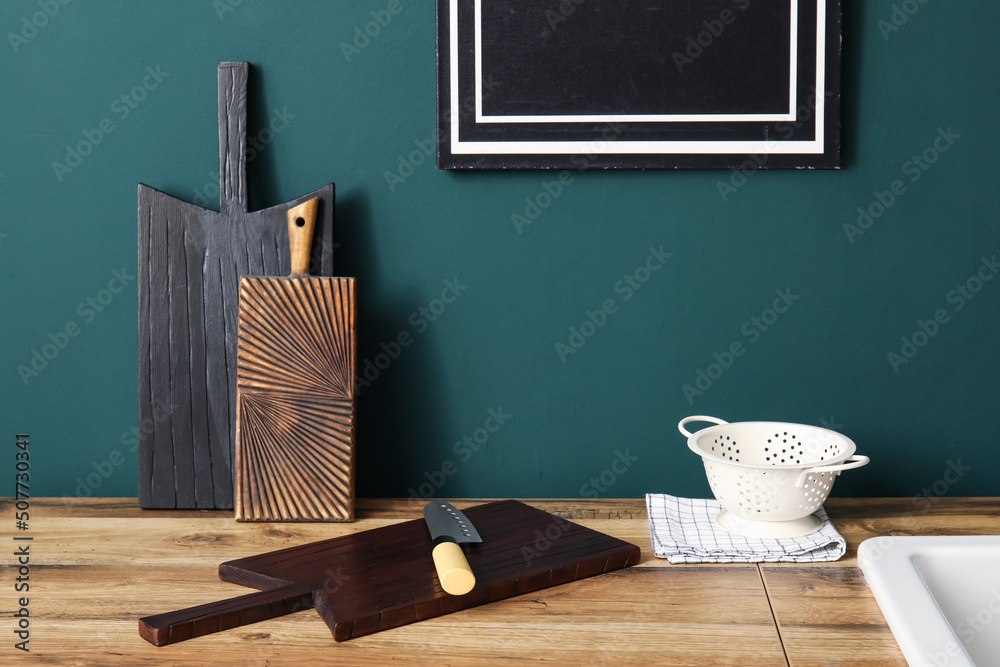 Cutting boards with knife and colander on counter near green wall