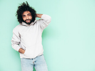 Handsome smiling hipster  model.Sexy unshaven Arabian man dressed in summer stylish hoodie clothes. Fashion male with long curly hairstyle posing near green wall in studio. Isolated