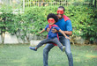 Happy funny African American father carrying little boy flying in superhero costume in garden at home. Happy loving Black African family playing together. Childhood and fun concept