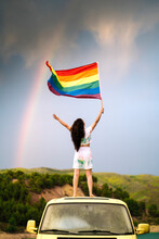 Young Woman Holding Rainbow Flag Standing On Van