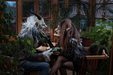 Krampus And Witch With Wineglass Holding Hands Sitting At Table