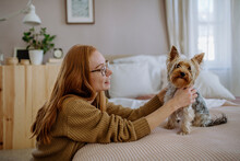 Smiling Woman Looking At Pet Dog Sitting On Bed At Home