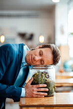Mature Businessman Leaning On Glass Container With Plant At Coffee Shop