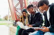 © Westend61 - Smiling young man using laptop sitting by friends on wall