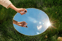 Perfumery And Nature Concept - Hand With Bottle Of Perfume And Sky Reflection In Round Mirror On Summer Field