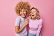Joyful happy young women laughs out gladfully dressed in casual clothes notice something funny giggle positively express positive emotions isolated over pink background. Authentic human feelings