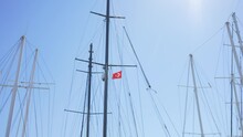 4k Stock Video Footage Of Many Black, White Tall Masts Of Many Yachts Isolated On Clear Sunny Blue Sky Background. National Red Flag Of Turkey Waving In Strong Wind