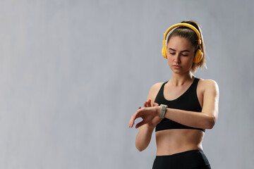 Fitness woman relaxing and listening music during her workout over grey background.