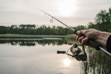 Wall Mural - Fisherman with rod, spinning reel on the river bank. Sunrise. Fishing for pike, perch, carp. Fog against the backdrop of lake. background Misty morning. wild nature. The concept of a rural getaway.