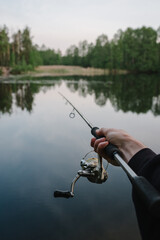 Wall Mural - Fishing day. Fishing for pike, and perch from a lake, river or pond. Background wild nature. Fisherman with rod, spinning reel catches fish from a pier or boat. Article about concept of rural getaway.