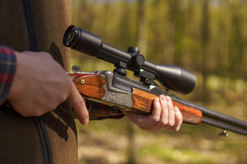 Close-up of hunter man waiting with rifle gun on prey in forest.