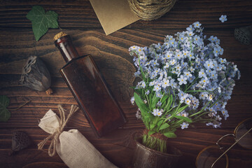 Wall Mural - Tincture or potion bottle, sachet of dried herbs, glasses, bouquet of wild forget me not flowers. Top view, flat lay.