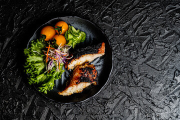 Grilled tilefish marinated with saikyo-miso and tomato salad on a black plate against a black design board.