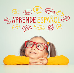 Beautiful cute little girl with eyeglasses looking at Learn Spanish text in Spanish and illustrations. English: Learn Spanish. Foreign language learning concept.
