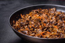 Fried Champignons With Carrots, Onions And Spices In A Pan Against A Dark Concrete Background