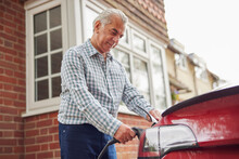 Mature Man Attaching Charging Cable To Environmentally Friendly Zero Emission Electric Car At Home