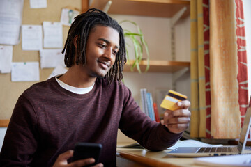 Male University Or College Student With Credit Card Making Online Purchase t At Desk In Room