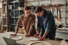 Portrait Of Two Artisan Shop Owners Designing Wooden Furniture In Workshop Interior