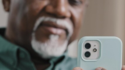 Unfocused unrecognizable mature elderly African 60s biracial man with gray beard using phone looking at smartphone screen American businessman male chatting mobile app e-commerce shopping browsing net