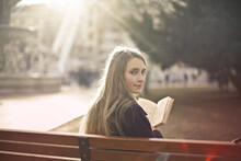Young Woman Reads A Book Sitting On A Bench