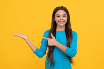 Canvas Print - happy child with long hair presenting product and point finger on copy space, advertisement.