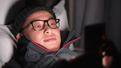 young chinese man lying and playing with mobile phone at night
