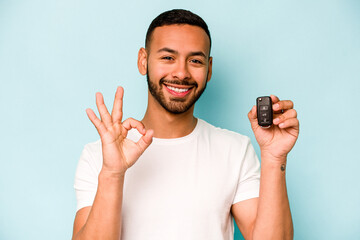 Wall Mural - Young hispanic man holding car keys isolated on blue background cheerful and confident showing ok gesture.