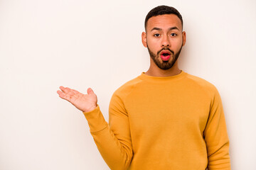 Wall Mural - Young hispanic man isolated on white background impressed holding copy space on palm.