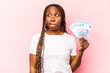 Young African American woman holding banknotes isolated on pink background confused, feels doubtful and unsure.