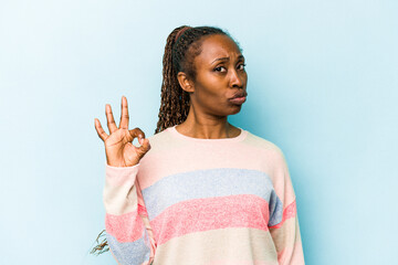 Young african american woman isolated on blue background winks an eye and holds an okay gesture with hand.