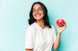 © Asier - Young hispanic woman holding an apple isolated on blue background looks aside smiling, cheerful and pleasant.