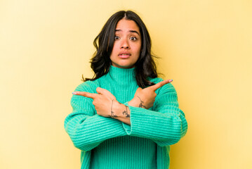 Young hispanic woman isolated on yellow background points sideways, is trying to choose between two options.