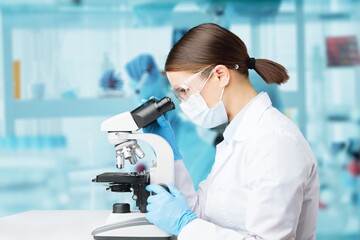 Poster - Young scientists conducting research investigations in a medical laboratory, a researcher in the foreground is using a microscope concept