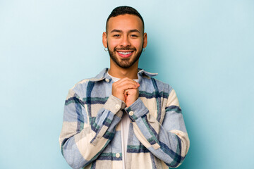 Wall Mural - Young hispanic man isolated on blue background praying for luck, amazed and opening mouth looking to front.