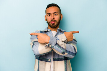 Wall Mural - Young hispanic man isolated on blue background points sideways, is trying to choose between two options.