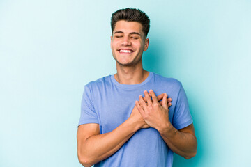 Young caucasian man isolated on blue background has friendly expression, pressing palm to chest. Love concept.