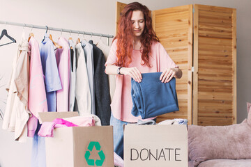 Wall Mural - Smiling young woman putting clothing into donation box