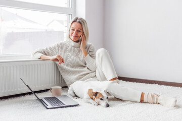 Wall Mural - Happy middle aged woman with dog using her laptop at cozy white home