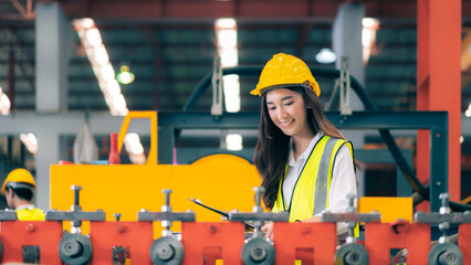 Happy professional beautiful Asian woman industrial engineer/worker/technician with safety hardhat use clipboard to inspect quality control of machinery in production steel manufacture factory plant