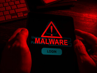 Hands in the dark hold a tablet with an inscription malware.